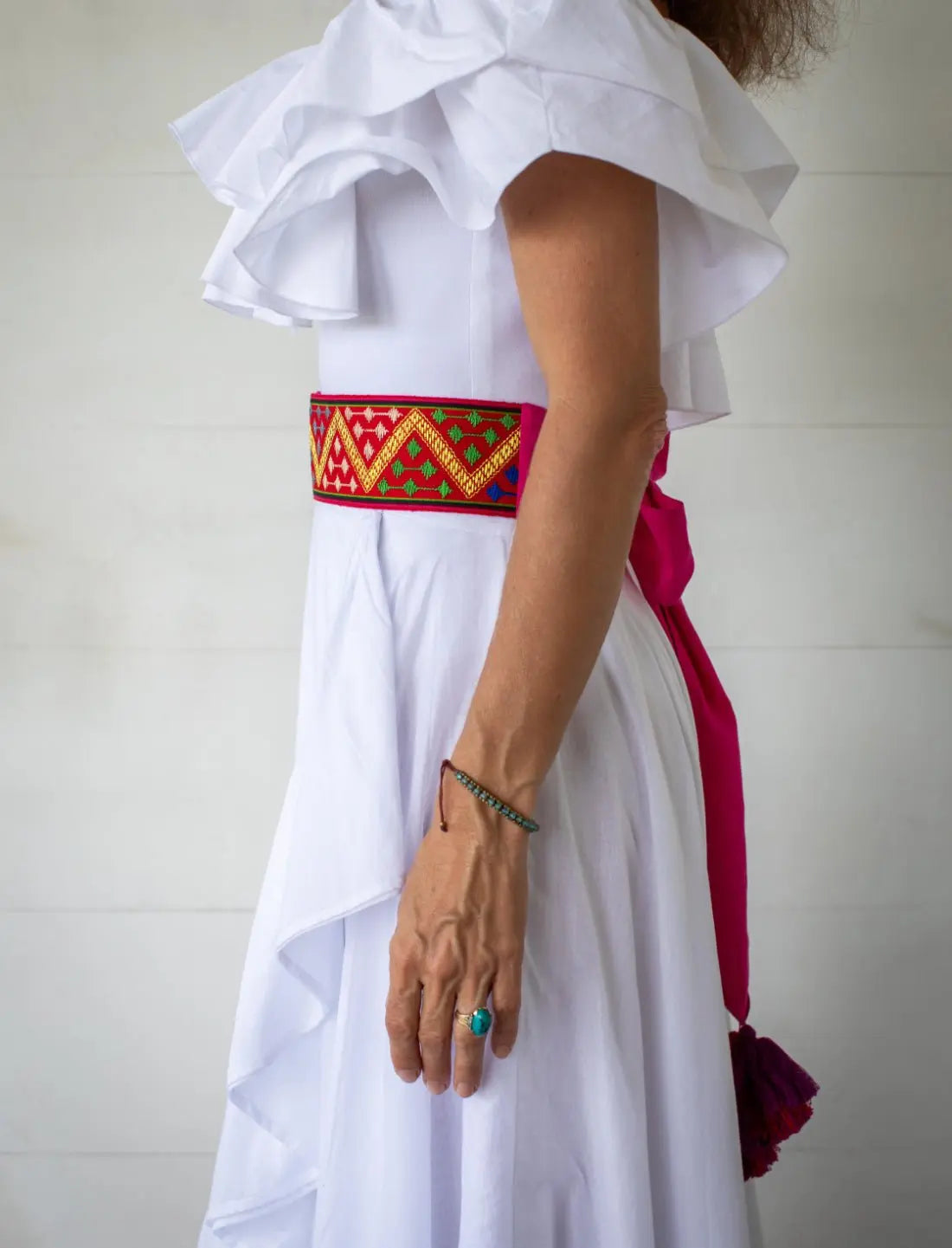 This image shows a side view of the Golden Dawn Embroidered Belt. It transitions from the embroidered weave to a pink cotton sash that ties in the back.